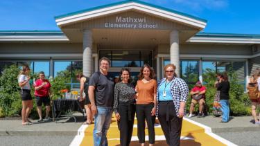 1 man and 3 female leadership team members pose in front of elementary school and on new orange crosswalk