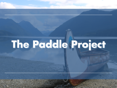 Scenic image of water and mountains with a canoe at shore. Blue overlay with title "The Paddle Project".