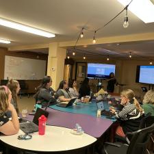 Group of adults sitting at tables learning from a female speaker